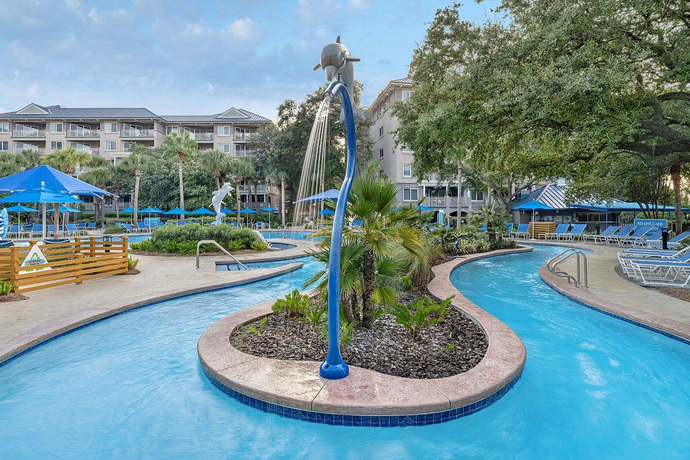 Resort-style lazy river pool with tropical landscaping and lounge seating