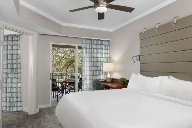 Bright king bedroom with private balcony, outdoor seating, and peaceful tree views