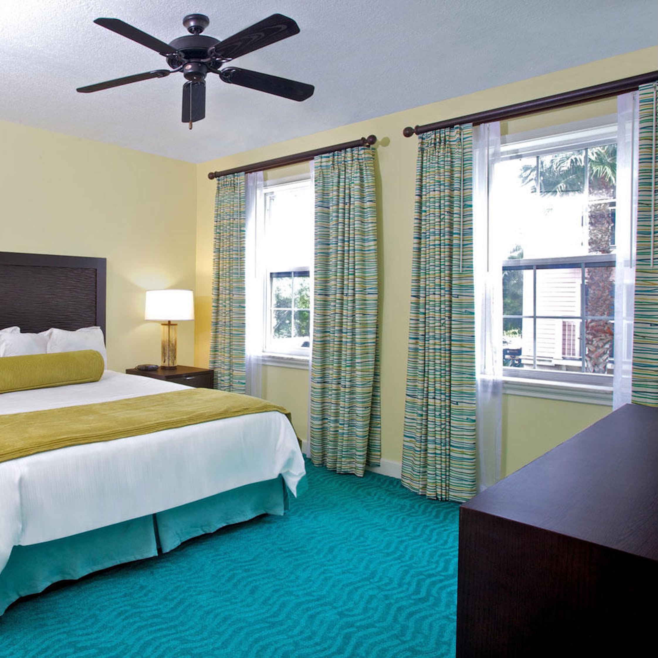 Bright coastal bedroom with large windows, ceiling fan, and cheerful decor