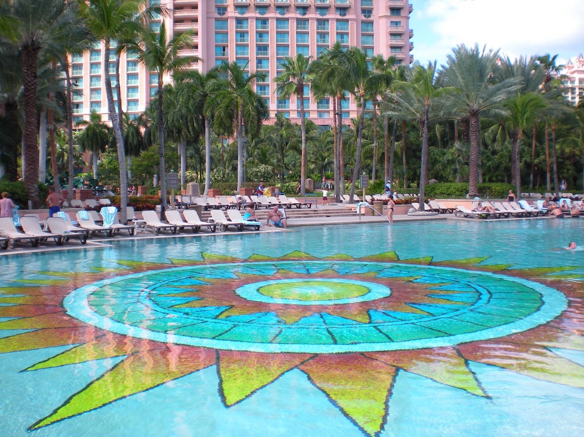 Tropical resort pool with sun mosaic, palm views, and plenty of loungers