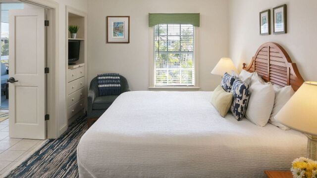 Bright coastal-style bedroom with king bed, sunny window, and cozy seating