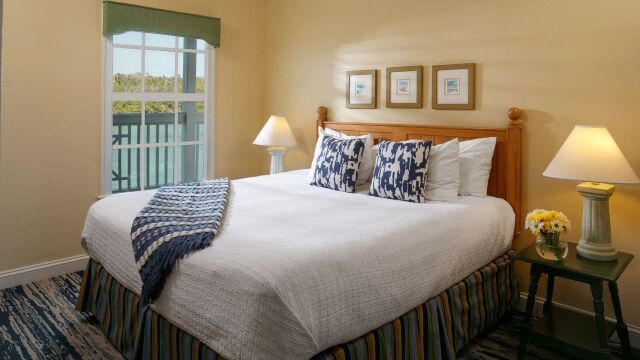Bright king bedroom with cozy coastal accents and balcony-view window