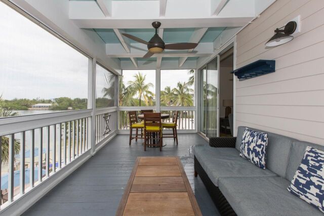 Screened waterfront porch with lounge seating, dining area & tropical views