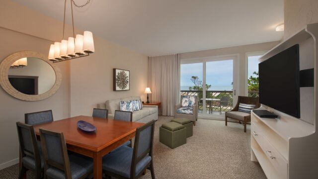 Bright living space with dining area, big TV, and private ocean-view balcony