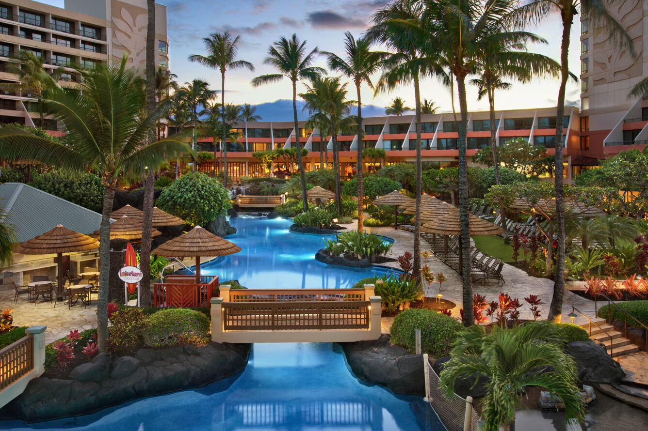 Tropical lagoon-style pool oasis with palms, bridge, and evening glow