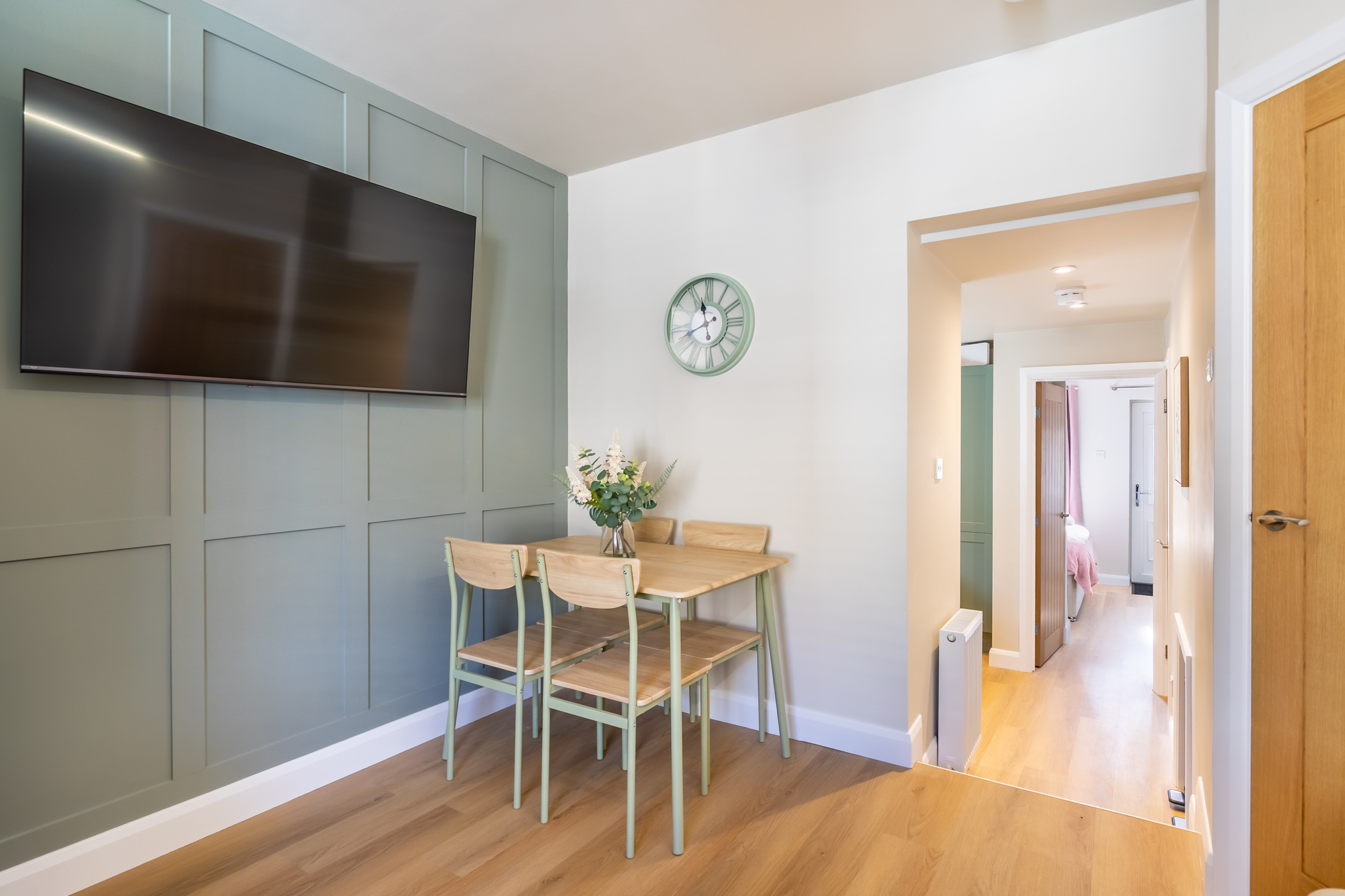 Bright dining nook with wall-mounted TV and stylish sage accent wall
