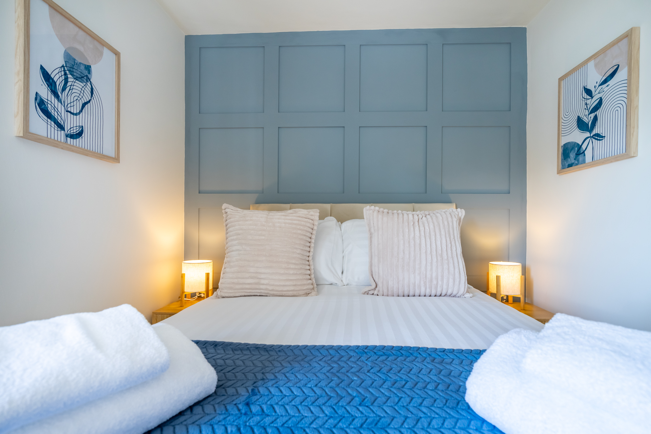 Cozy bedroom with blue accent wall, soft lighting, and fresh towels
