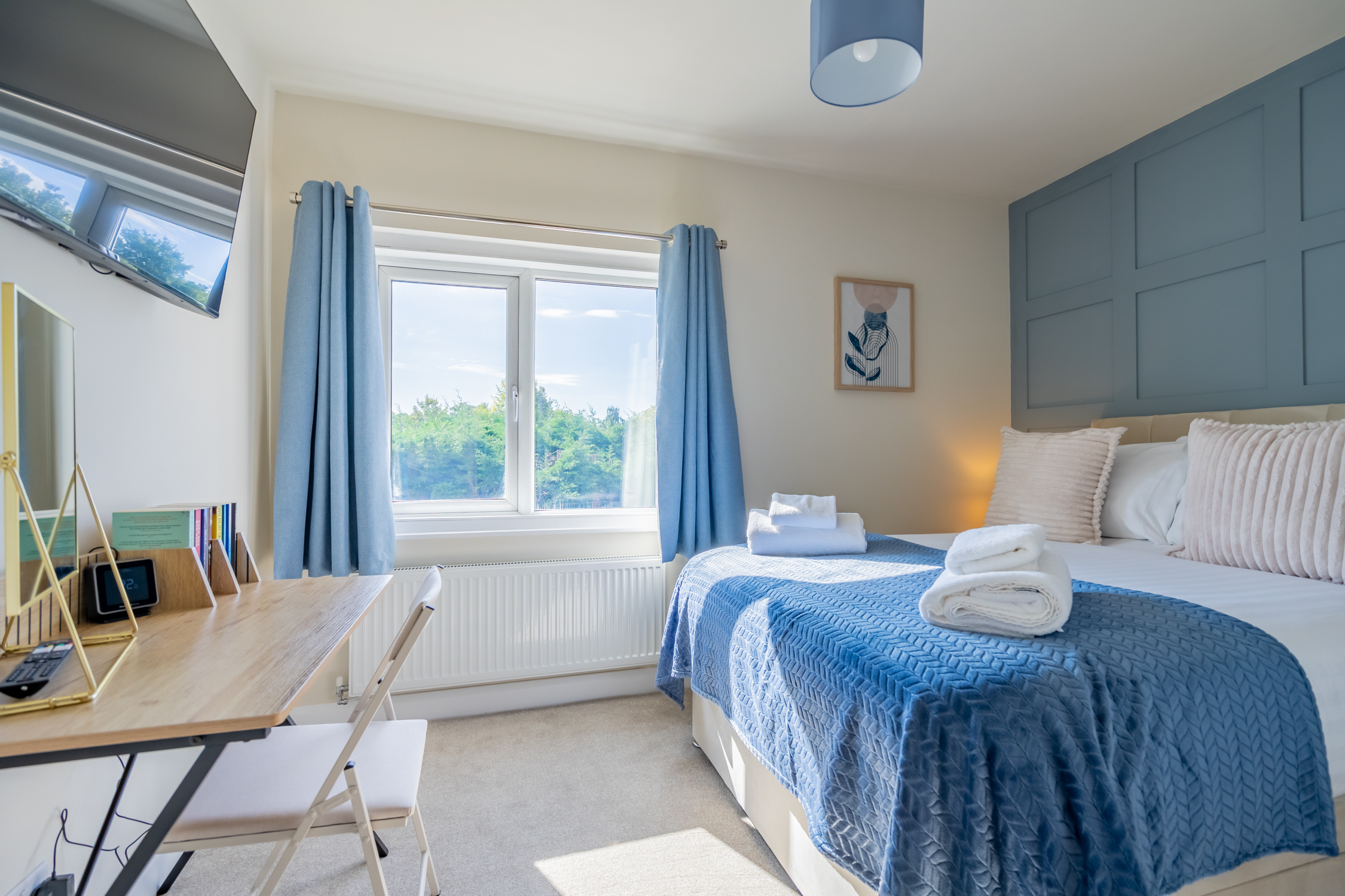 Bright, stylish bedroom with workspace, TV, and peaceful green views