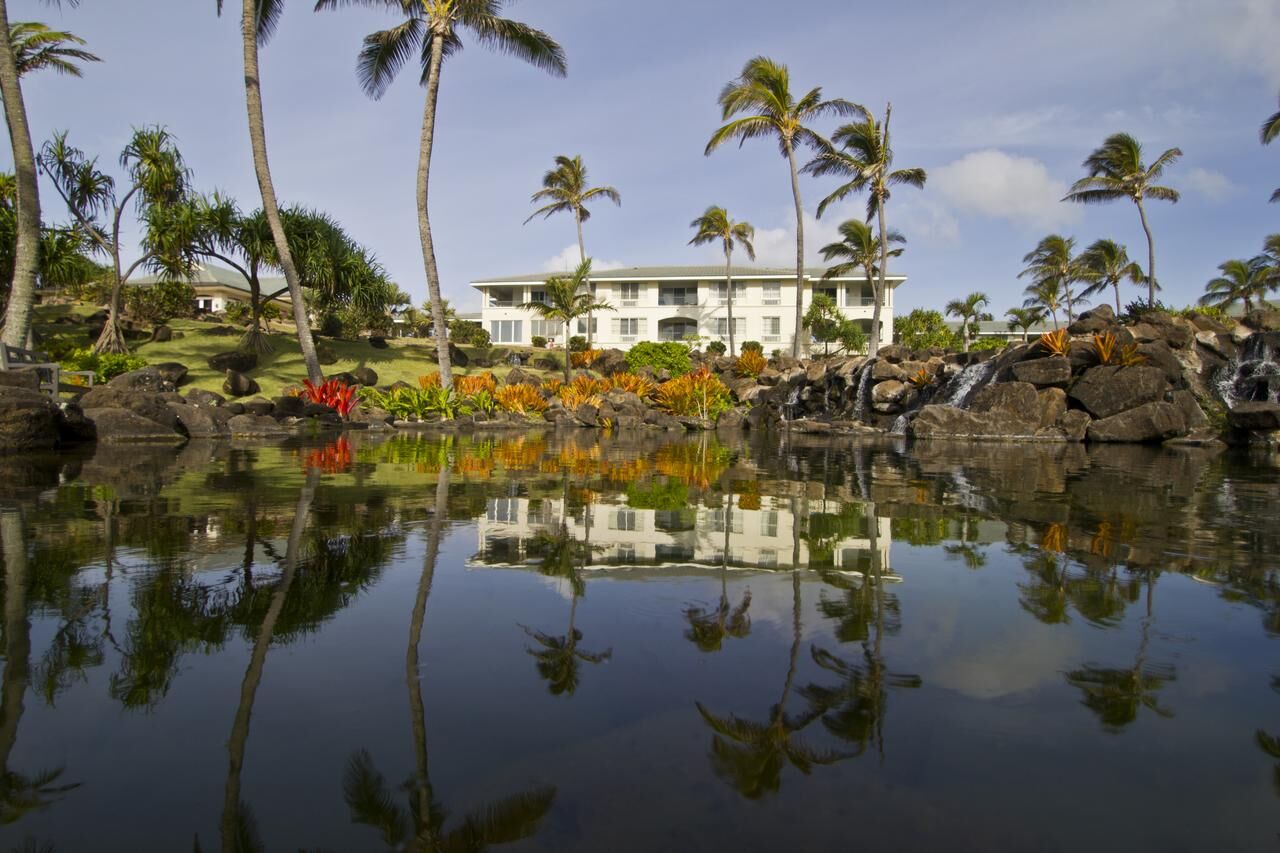 Tropical villa with palm-lined pond, waterfall, and serene reflections