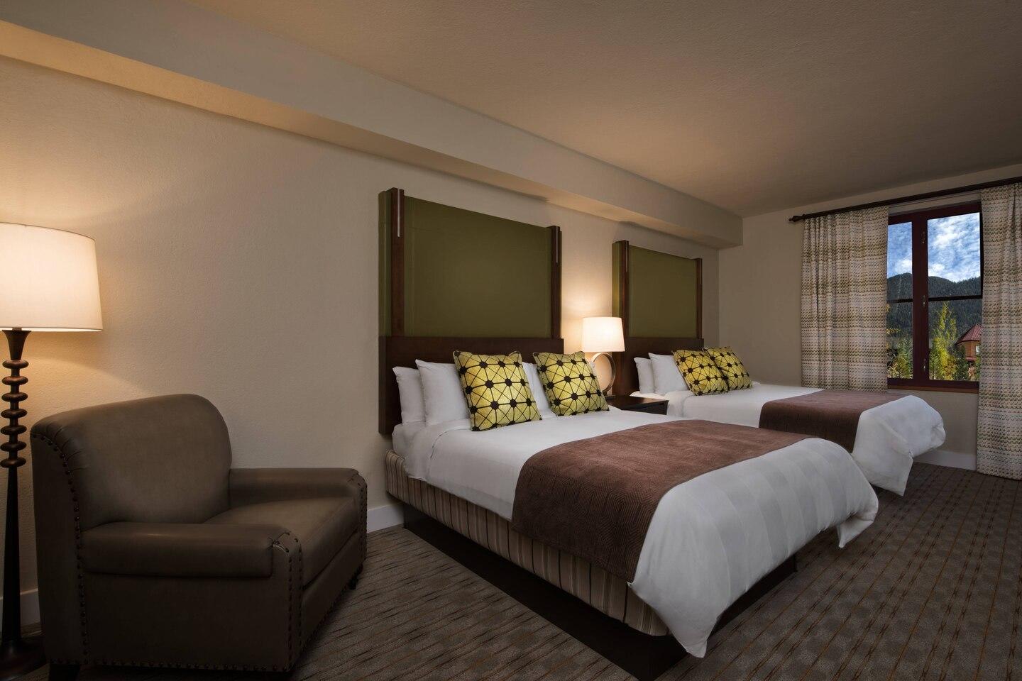Spacious double-queen room with cozy seating and mountain-view window