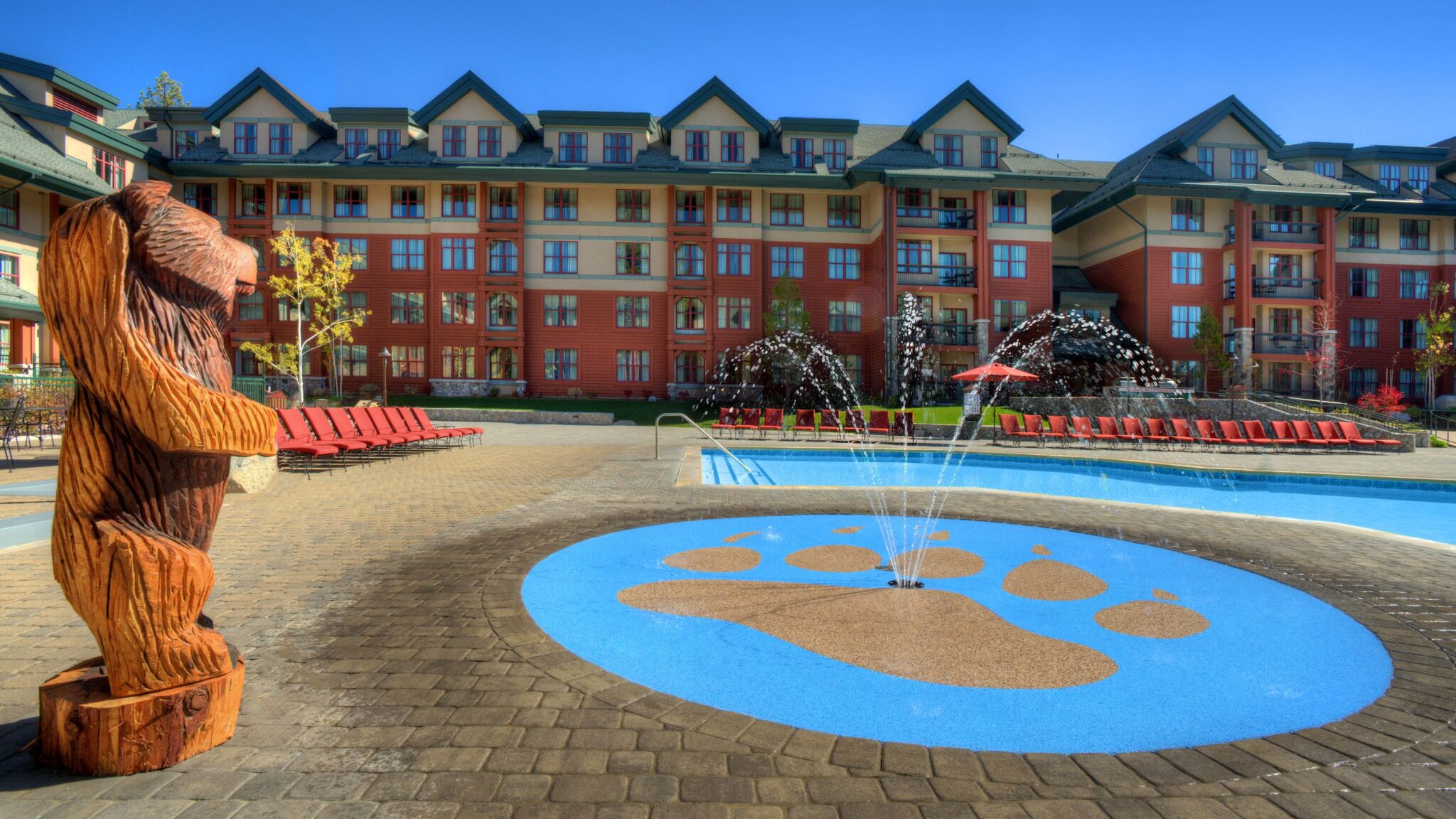 Resort-style pool deck with splash pad, loungers, and charming lodge views