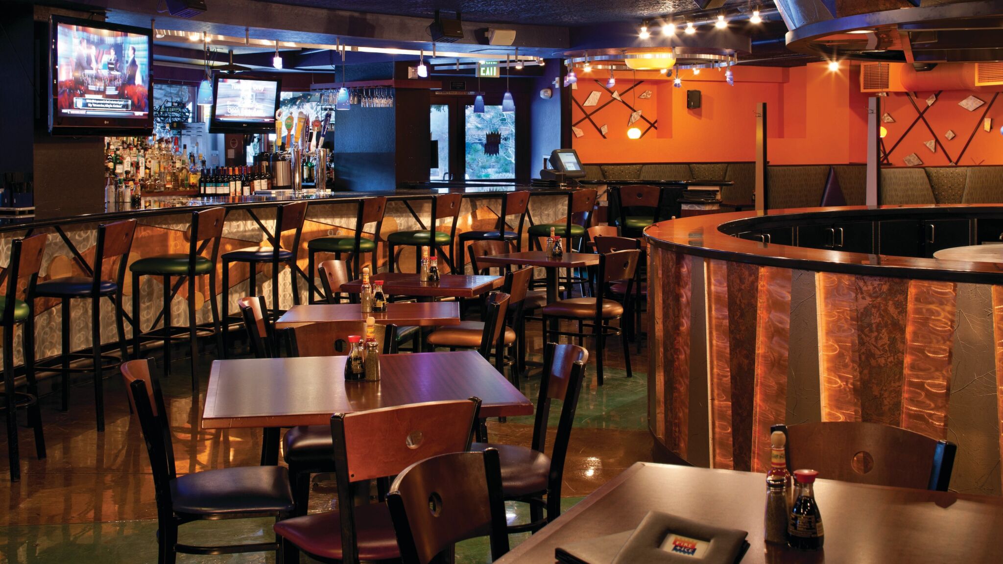 Chic on-site bar and lounge with dining tables, TVs, and warm ambiance