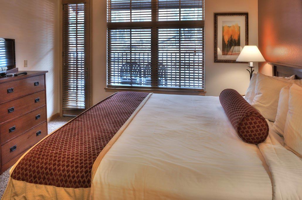 Cozy king bedroom with warm lighting, large windows, and in-room TV