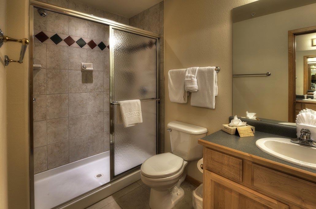 Clean tiled bathroom with walk-in shower and warm wood vanity