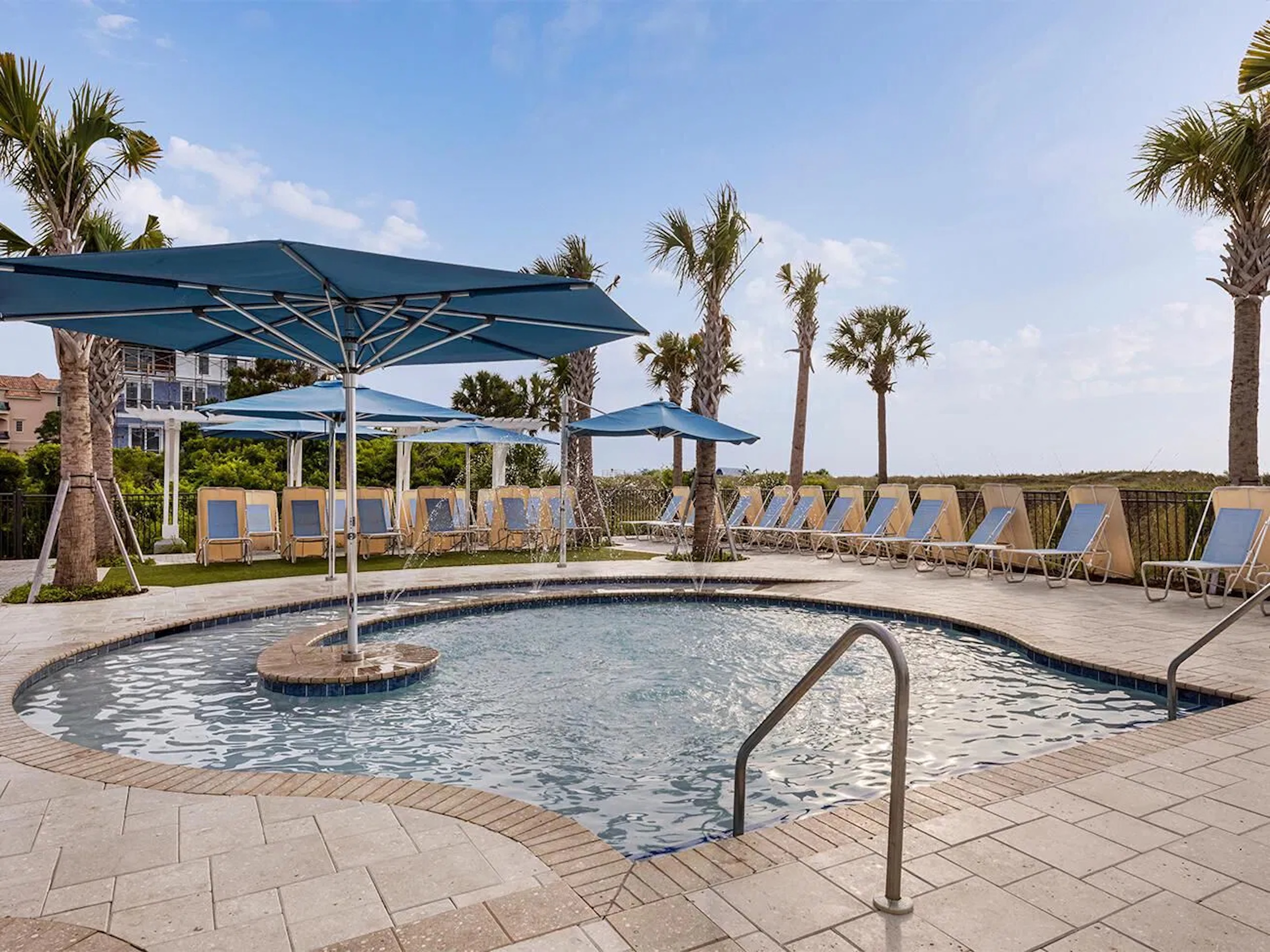 Resort-style pool with shaded loungers and breezy palm-lined views