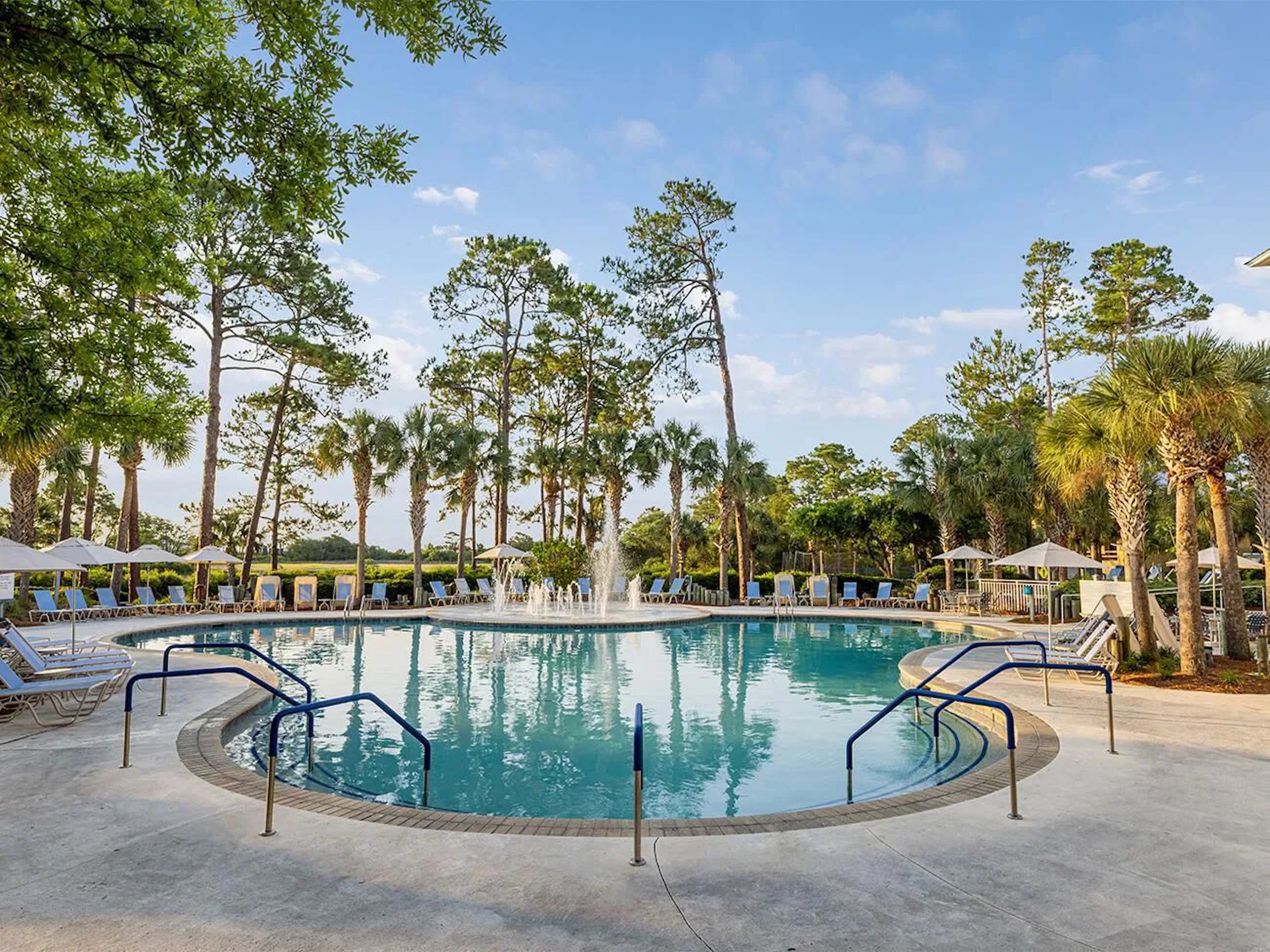 Resort-style pool with fountain, loungers, and tropical surroundings