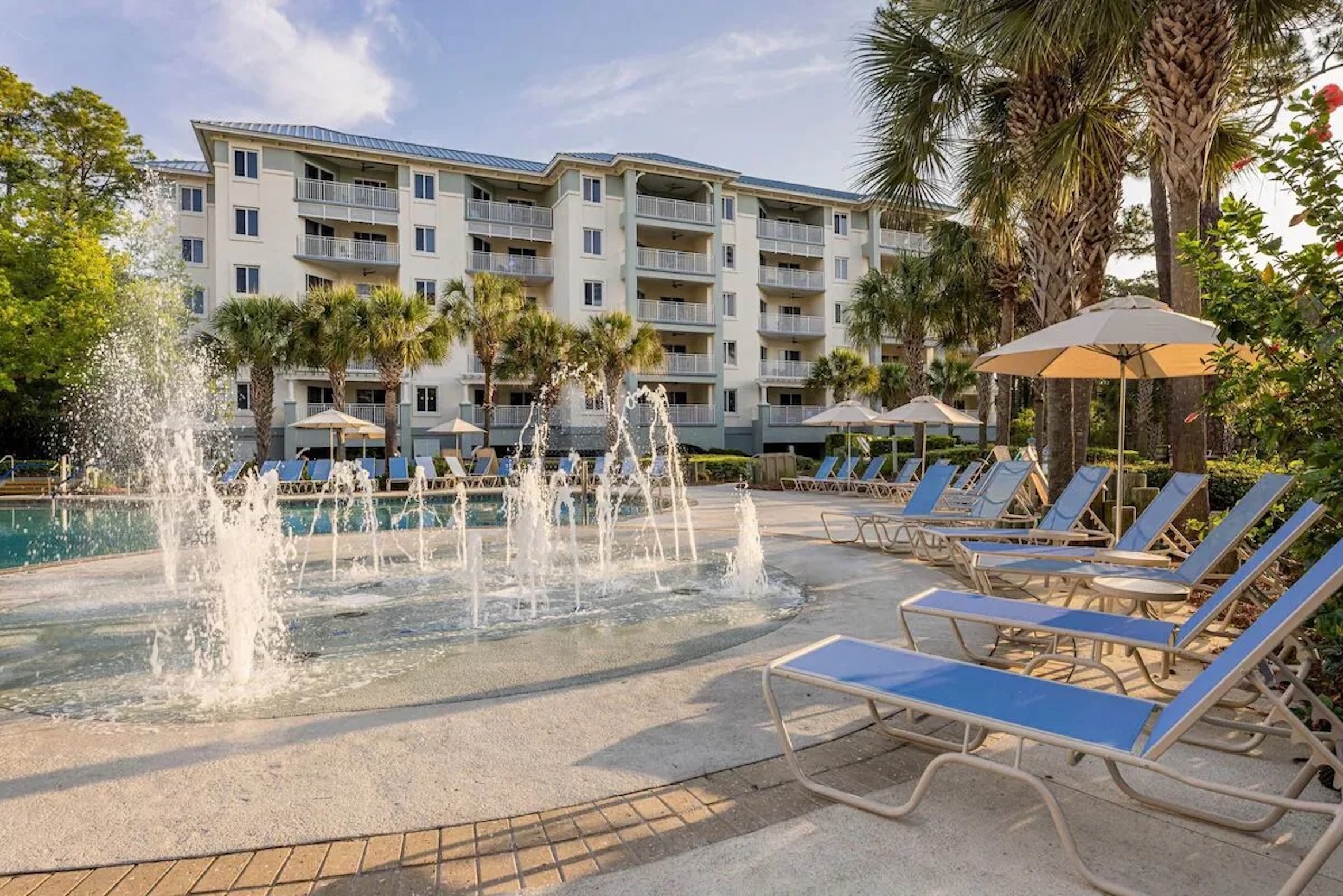 Resort-style pool with fountains, palm trees, and relaxing lounge seating
