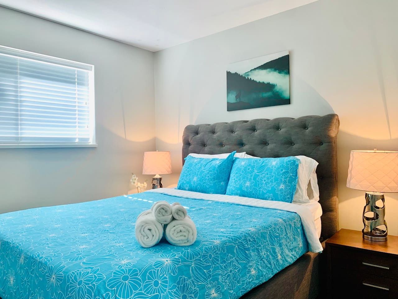 This bedroom has a queen bed that includes two side tables, two lamps and a closet with hangers.
