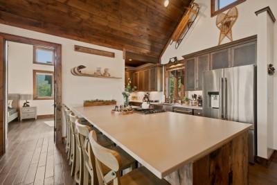 This gourmet kitchen impresses with soaring wood-plank ceilings and a spacious island lined with stool seating — vintage snowshoes and a hand-painted welcome sign add rustic charm to every gathering.
