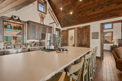Settle onto weathered barstools along the oversized island, where rustic ski and sled decor sets a playful tone — the open layout flows straight into a sunlit living room built for lazy mountain mornings.