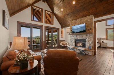 Gather in the great room beneath vaulted wood ceilings, where a stone fireplace anchors the space and mountain views stretch beyond every window — the natural heart of the home for cool evenings together.