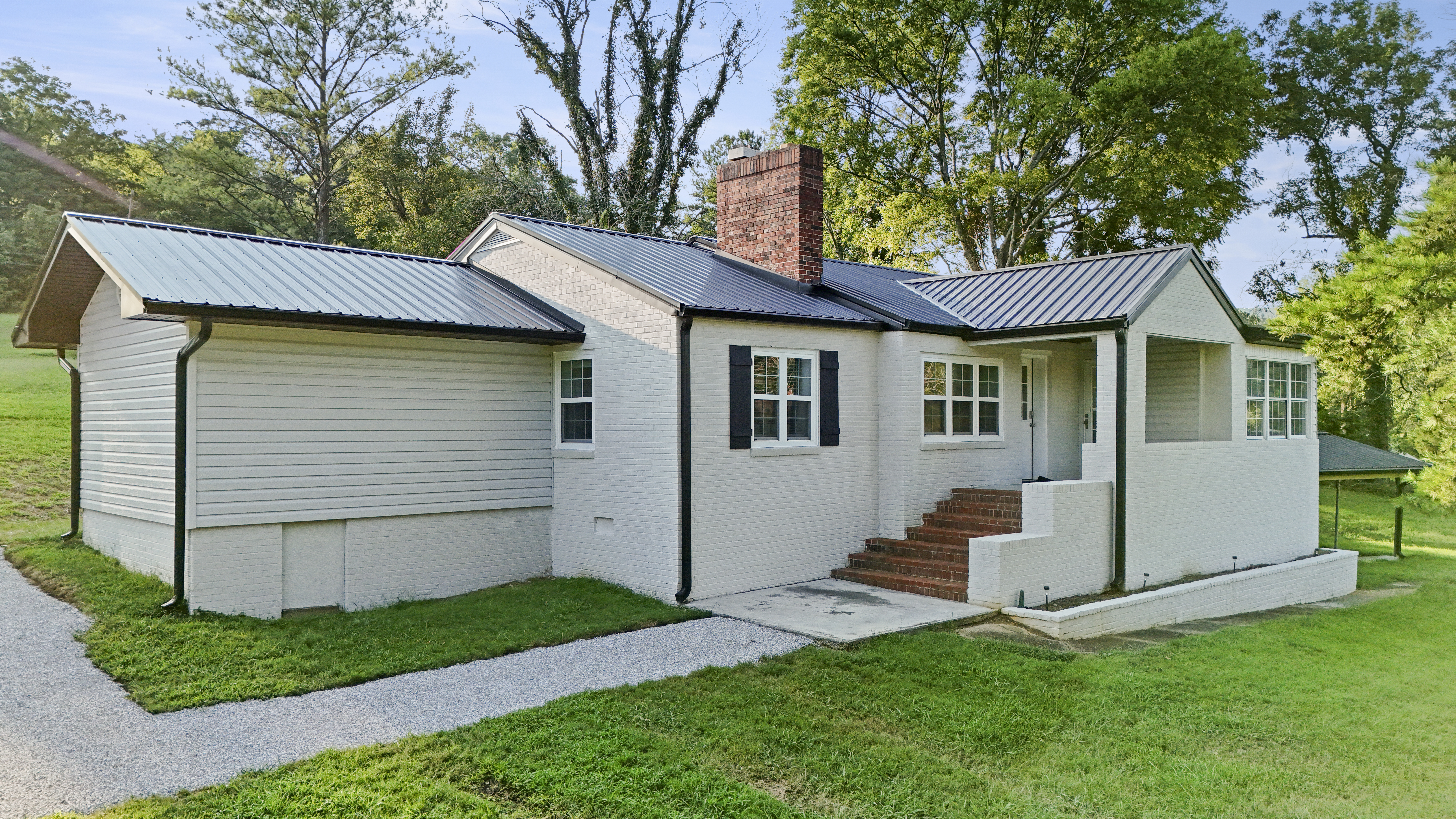 Charming white brick cottage with metal roof and peaceful tree-lined yard