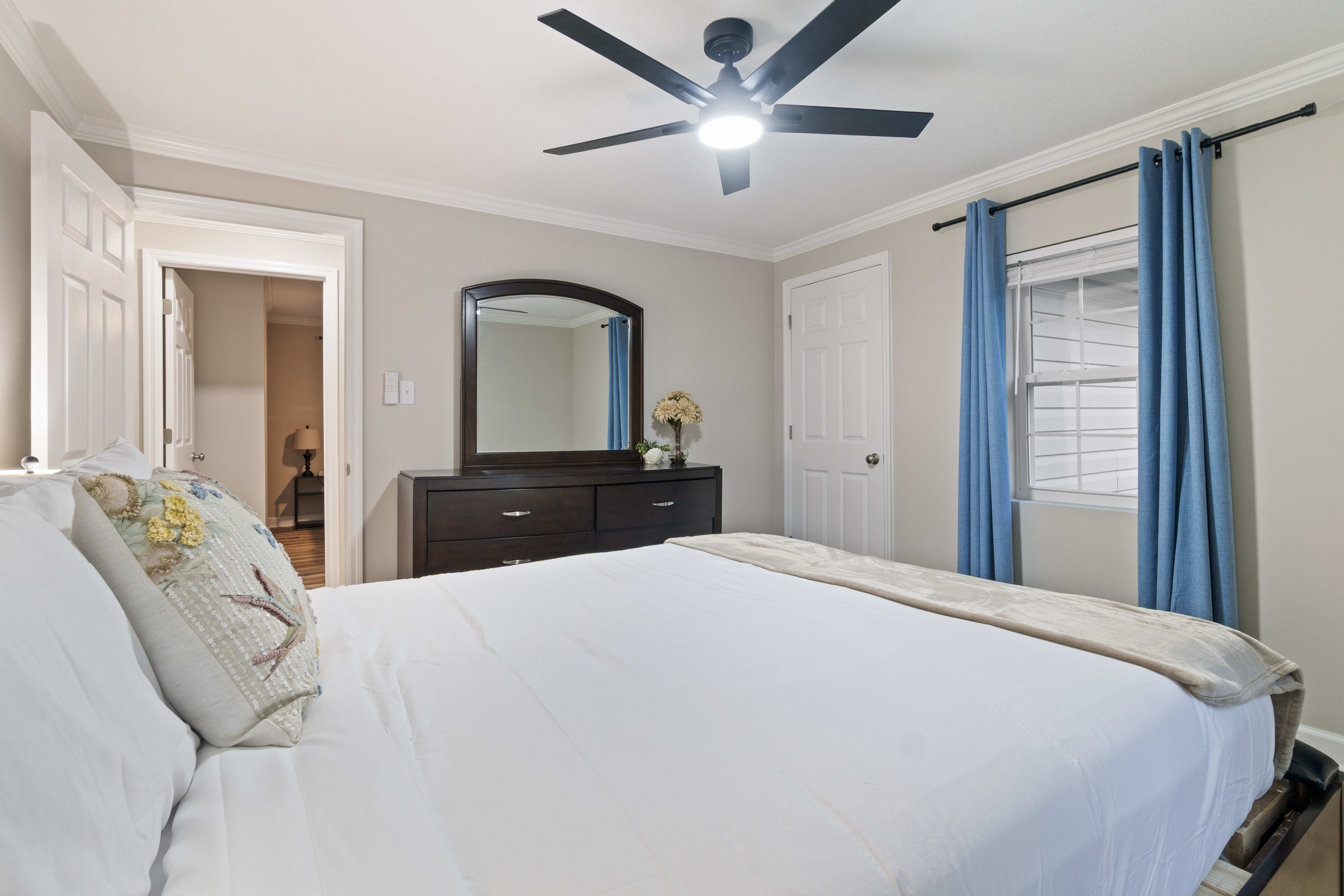 Bright, cozy bedroom with plush bedding, ceiling fan, and calming blue accents