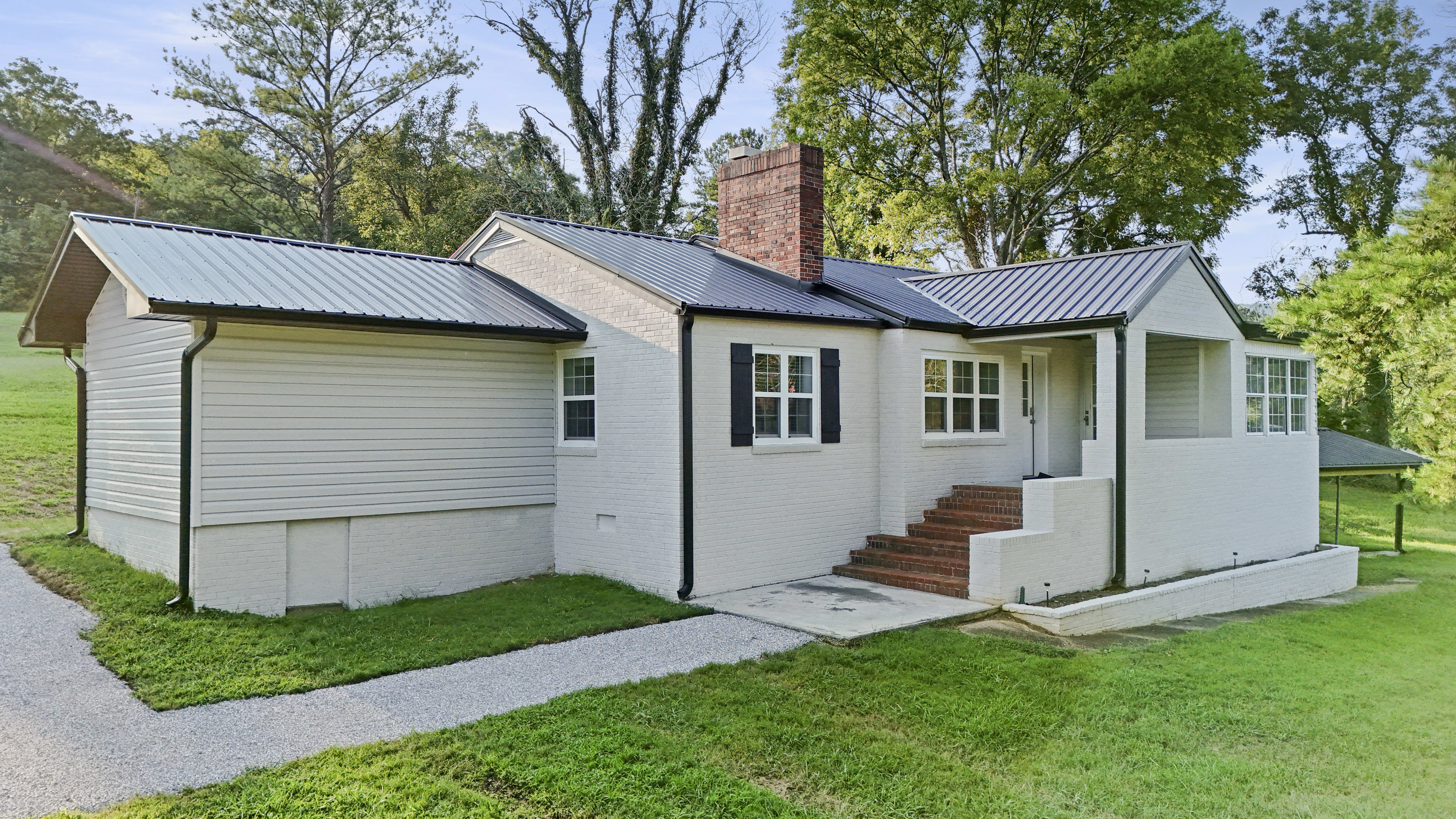 Charming white cottage with metal roof, lush lawn, and peaceful setting