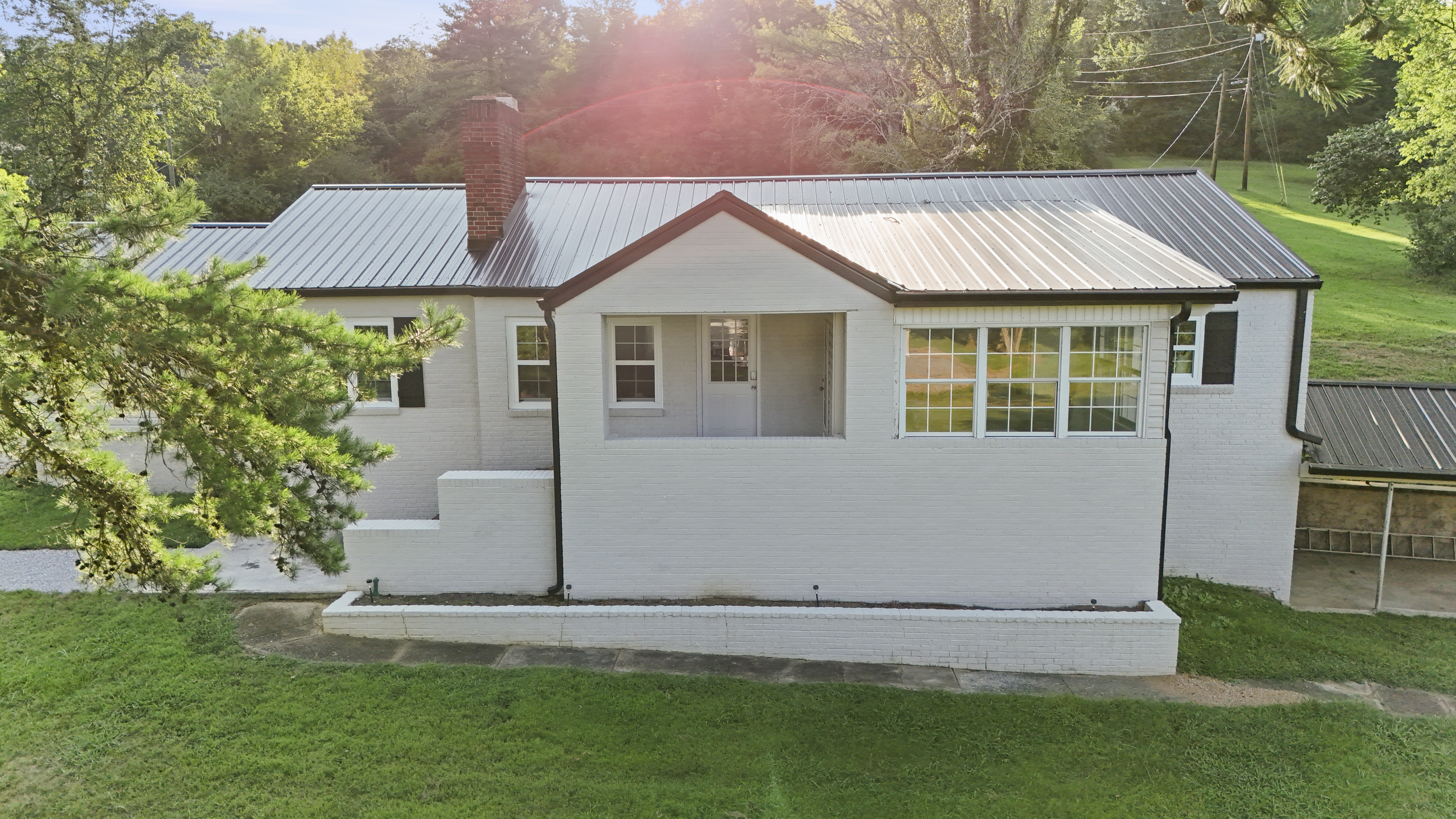 Charming white cottage with metal roof, big windows, and peaceful green setting