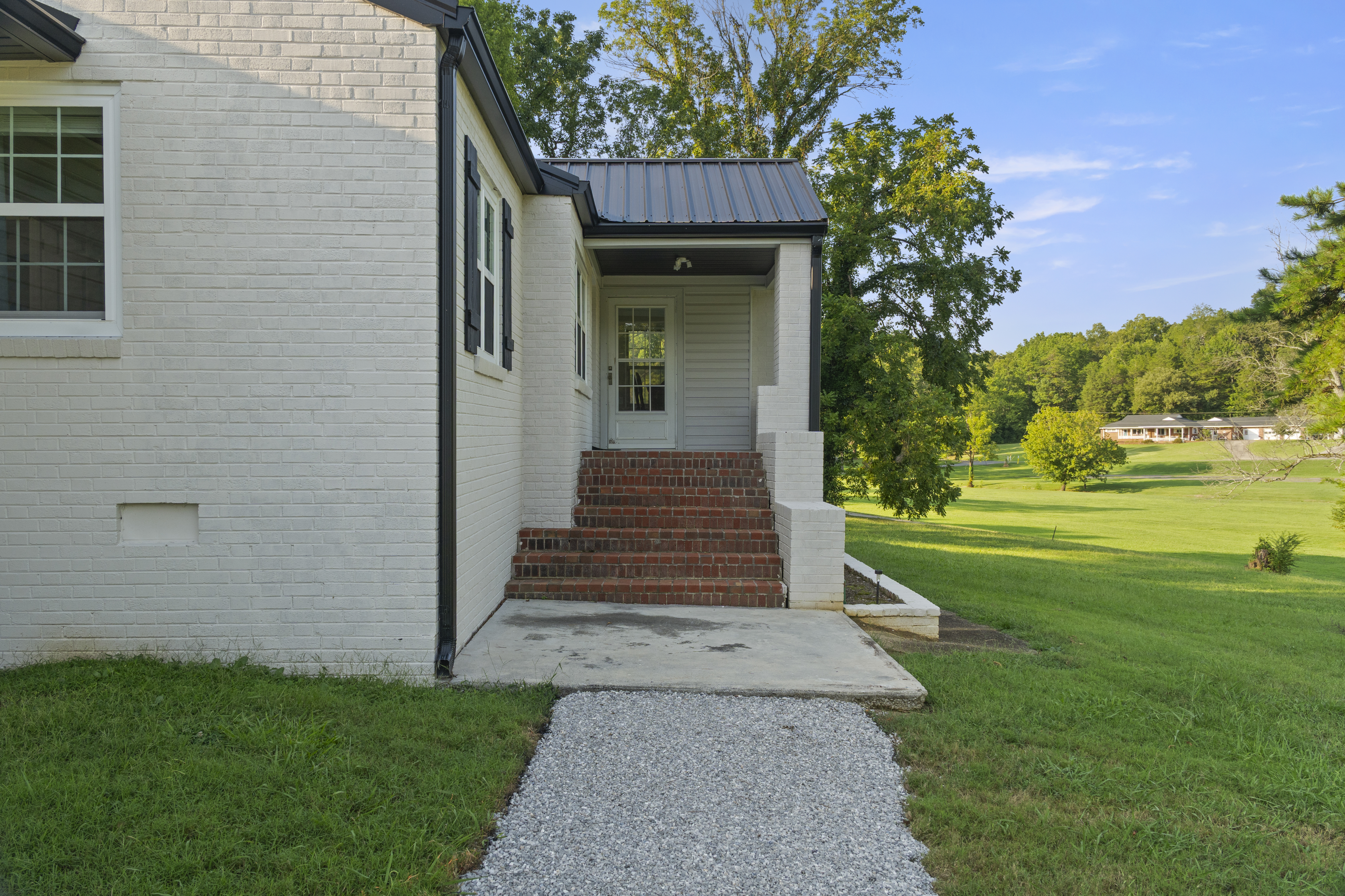 Charming covered side entry with brick steps and expansive green lawn