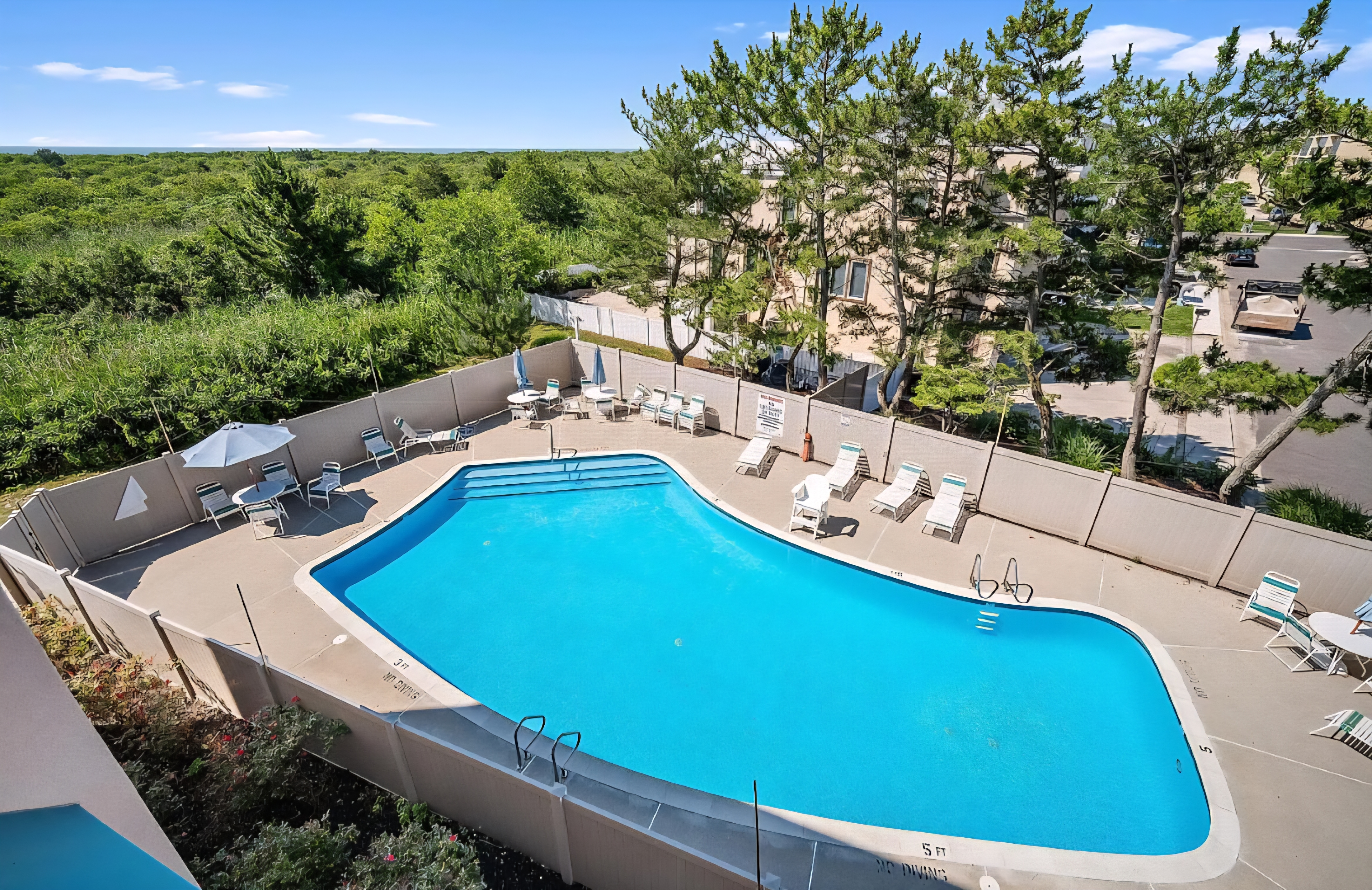 Spacious outdoor pool with loungers, tables, and peaceful tree-lined views