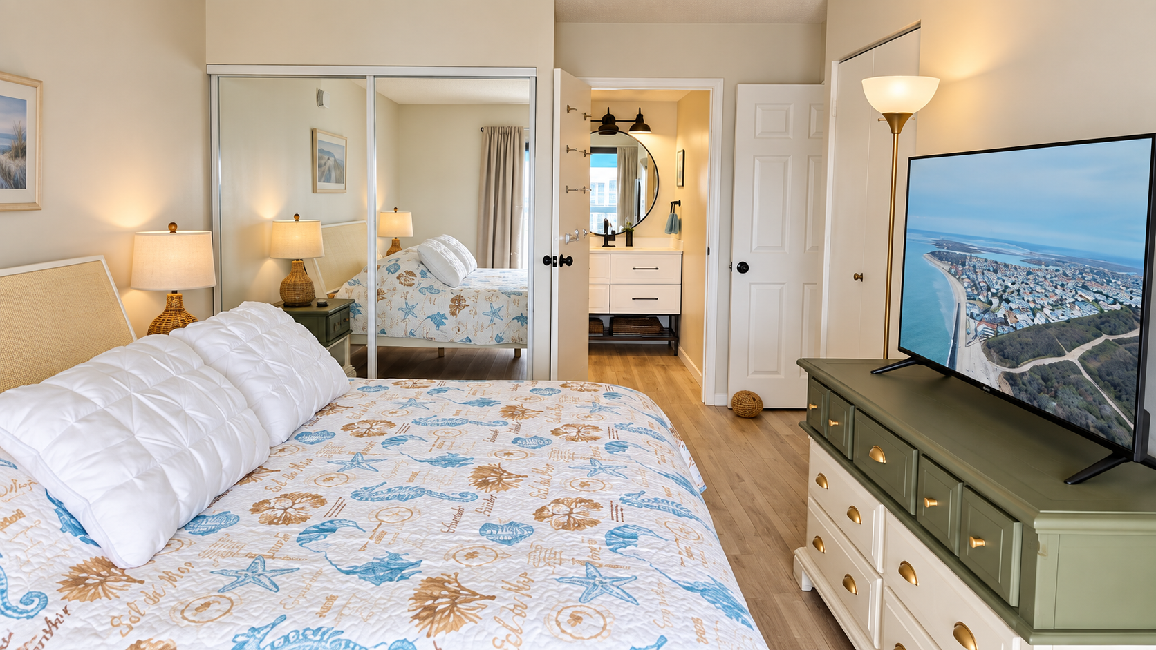 Bright coastal bedroom with TV, mirrored closet, and en suite vanity