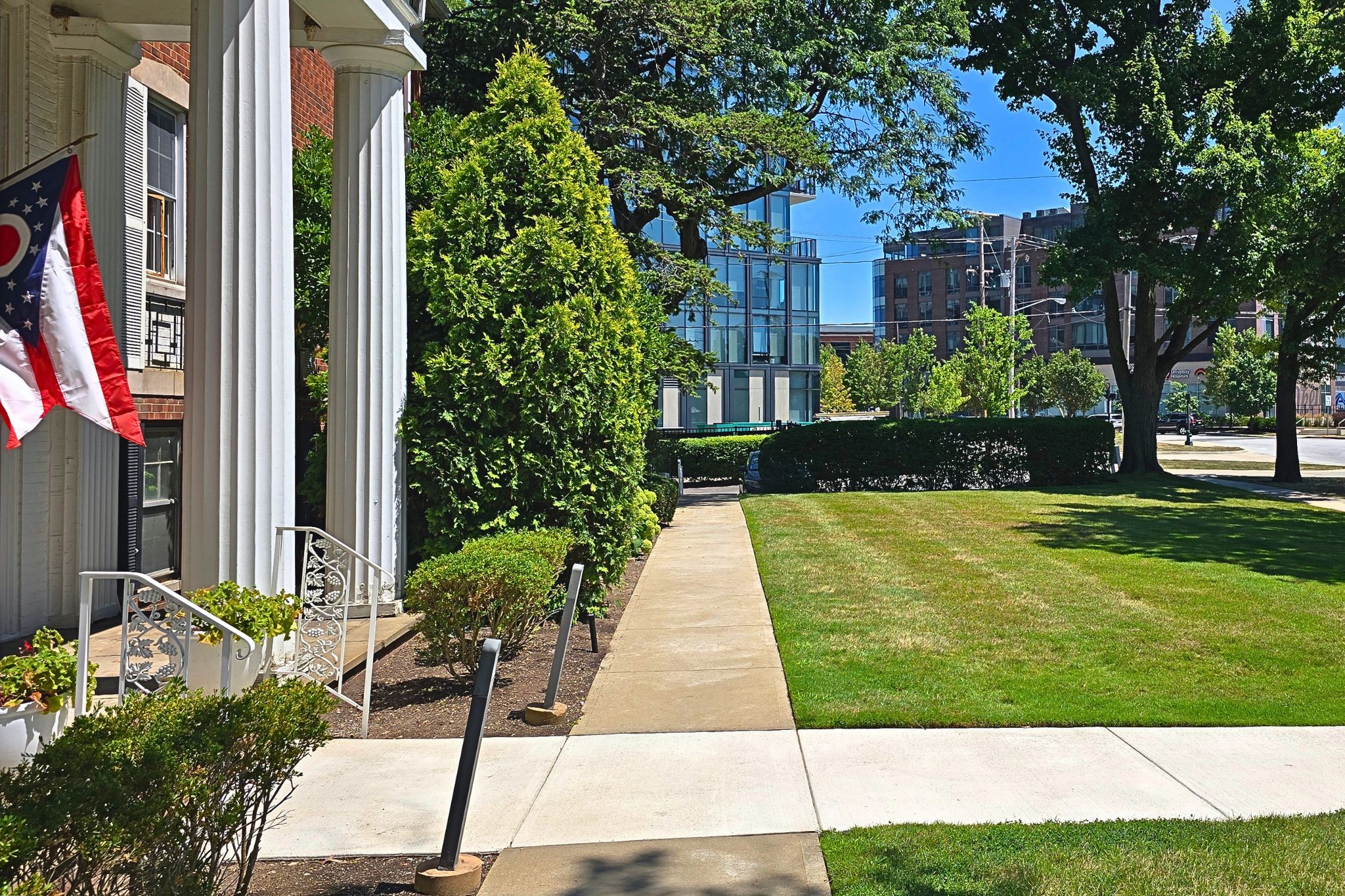 Elegant entry with grand columns, lush lawn, and sunny city surroundings
