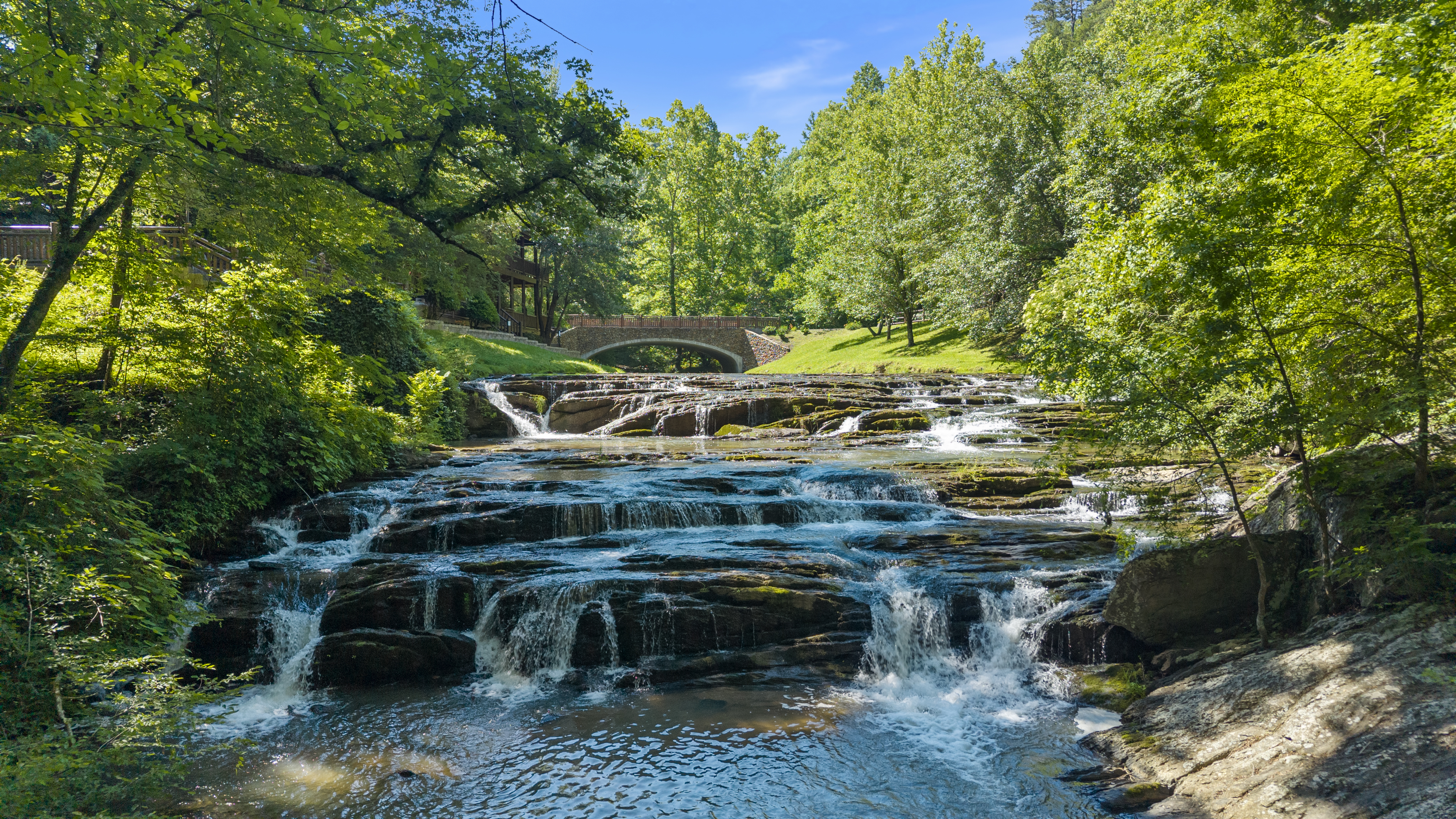 The community waterfall and stone bridge framed by greenery.