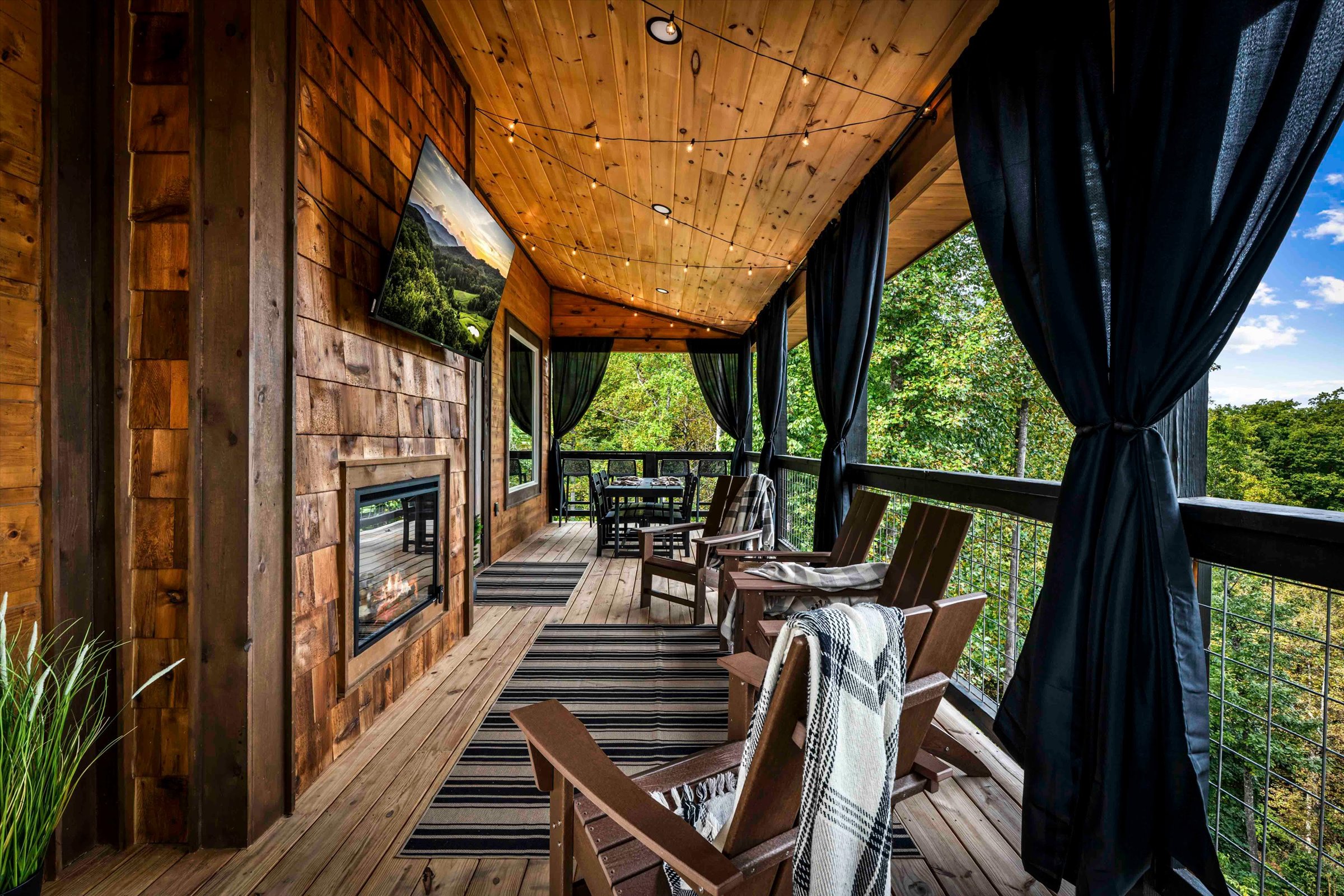 Covered mountain-view deck with fireplace, TV, dining area, and cozy seating