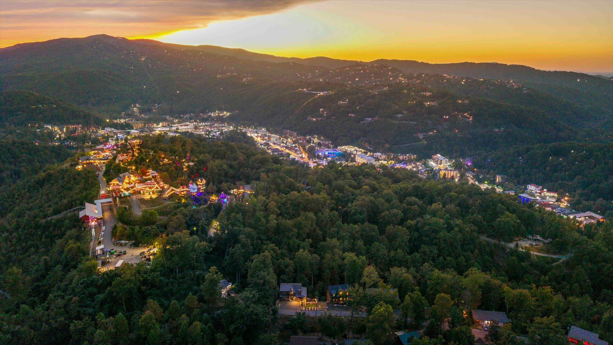 Sunset mountain-town views surrounded by forested hills and twinkling lights