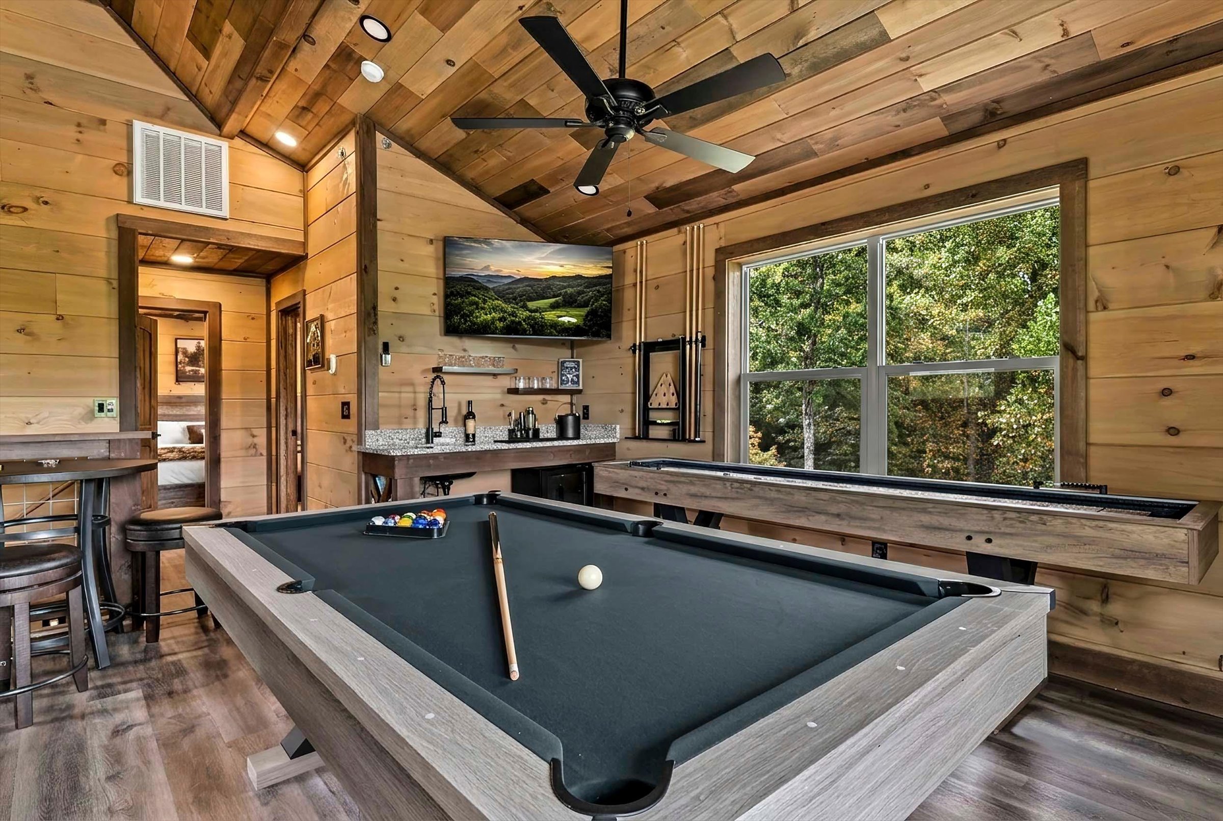 Rustic game room with pool table, wet bar, TV, and scenic forest views