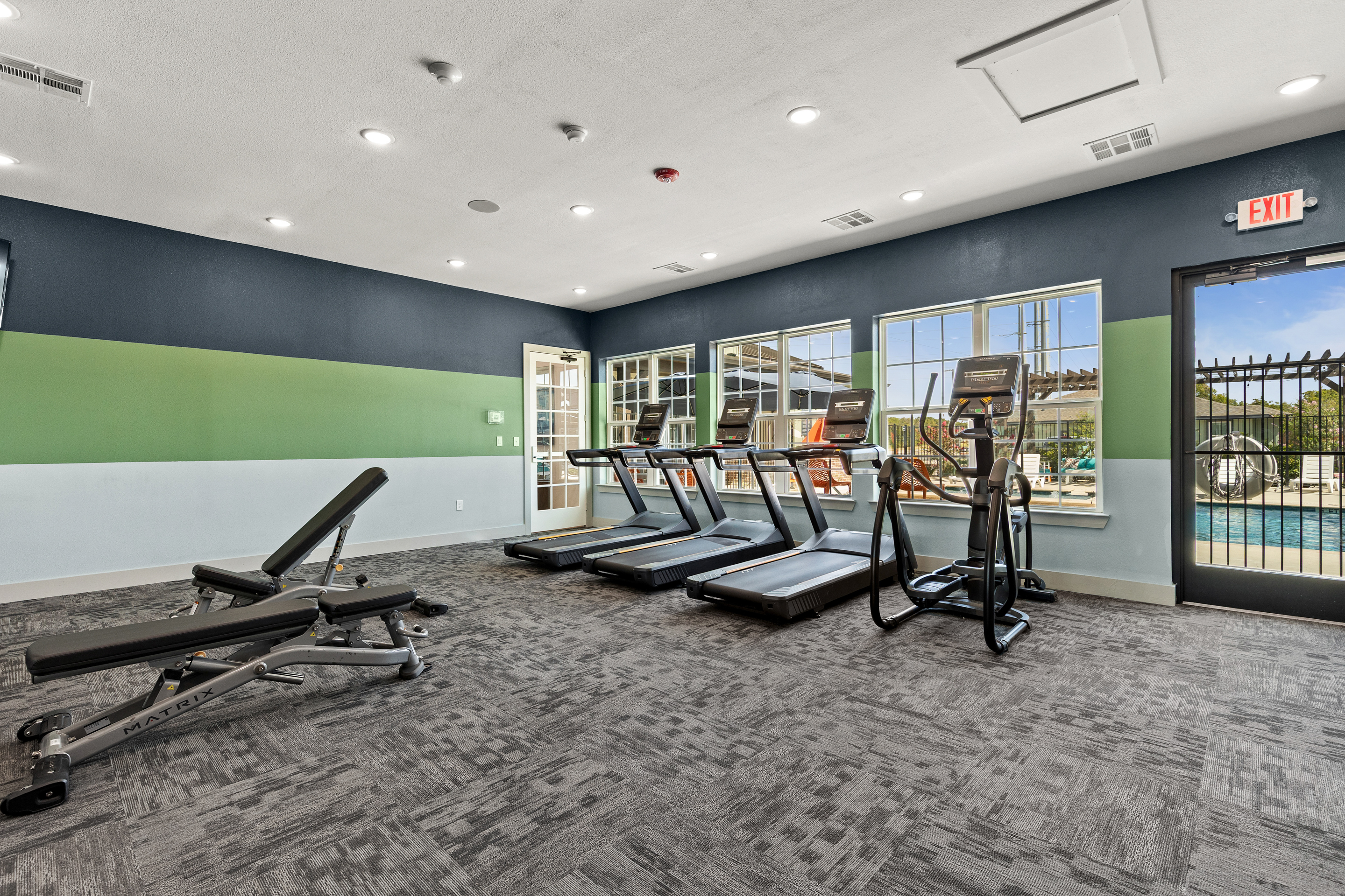 Bright on-site fitness room with cardio equipment and pool views