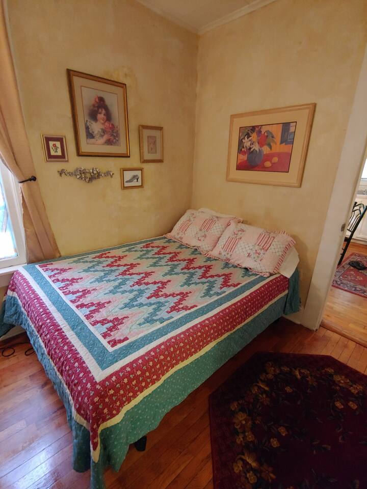 Another picture of the bedroom in natural daylight with the curtains open. Bedroom has a small rug by bed. We use various quilts and shams -just like staying at mom's or grandma's house. Bedding decor will vary.
