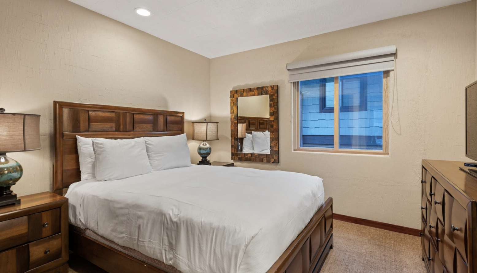 Cozy bedroom with plush king bed, warm wood furnishings, and soft lighting