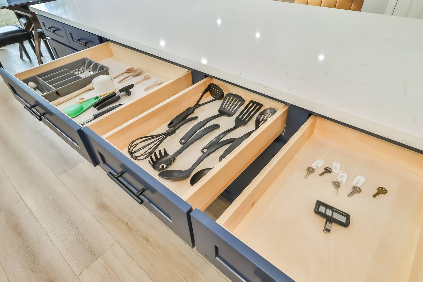 Gourmet kitchen featuring white shaker cabinetry, stainless steel appliances, a large navy blue island with a breakfast bar, and designer pendant lighting.