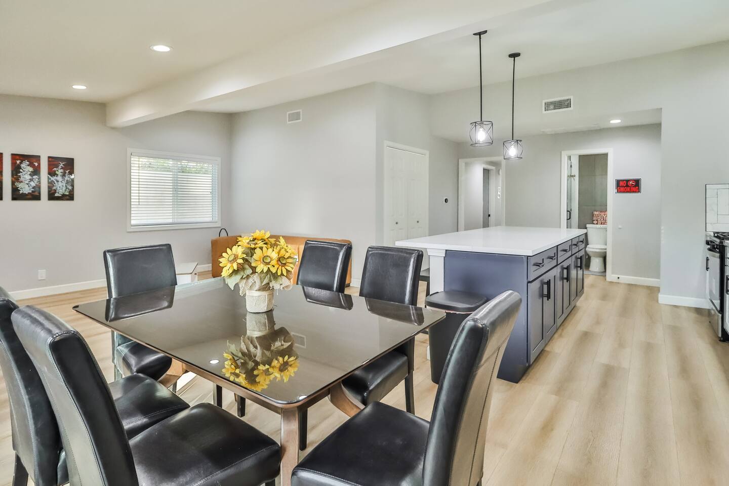 Bright dining space featuring a glass-top table with seating for six, luxury vinyl plank flooring, and a seamless transition to the kitchen and living areas.