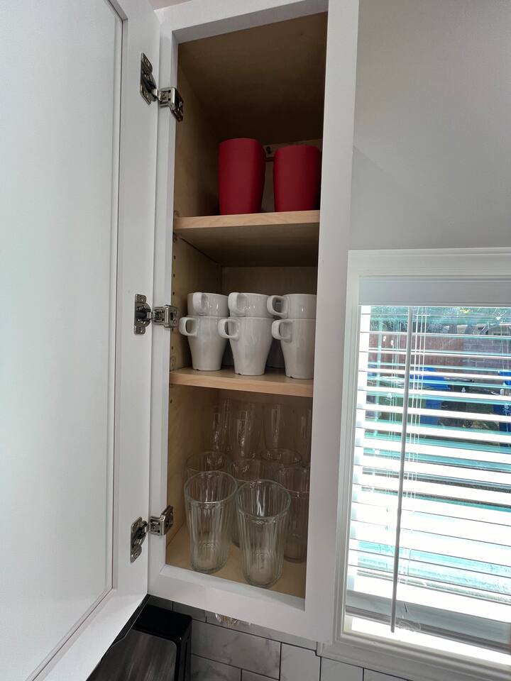 Fully stocked kitchen cabinets featuring white shaker doors, organized dishware and mugs, and a modern marble-patterned backsplash.