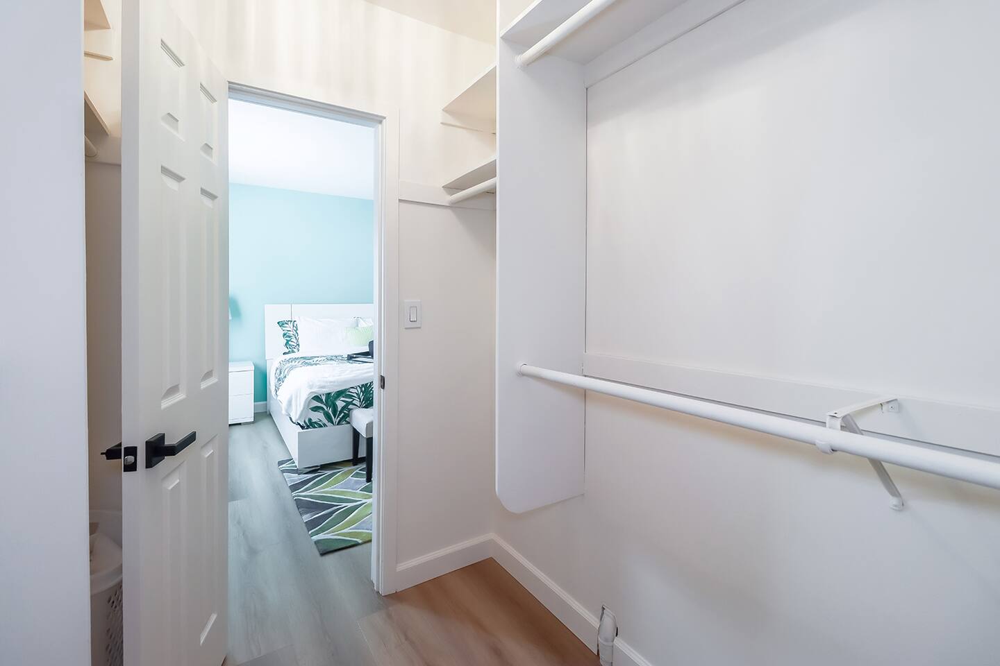 Clean Walk-In Closet with White Shelving & View into a Tropical-Themed Bedroom – Designed for Ease & Style