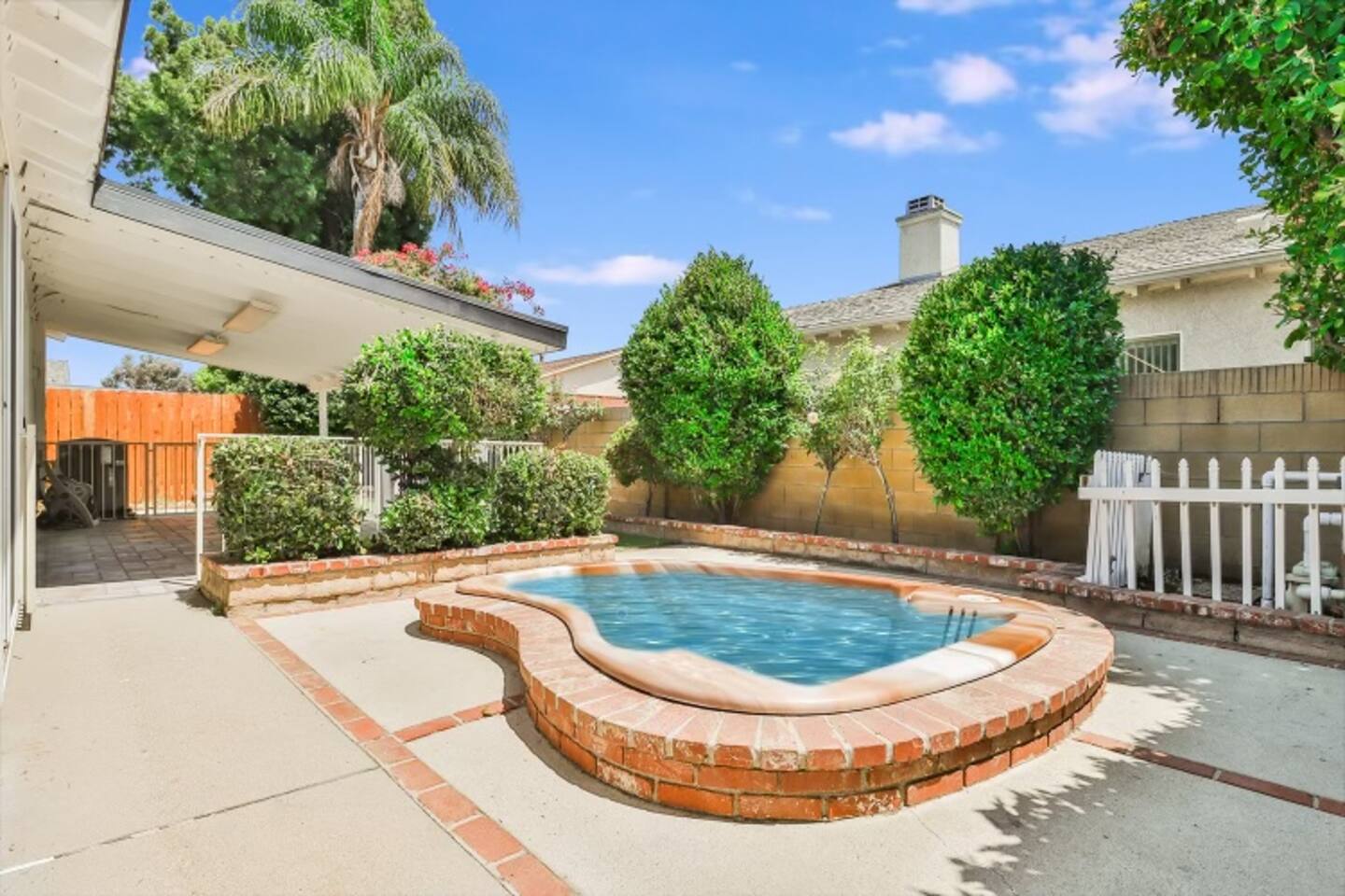 That inviting backyard jacuzzi with a red brick border, surrounded by a concrete patio with brick accents and lush green landscaping.