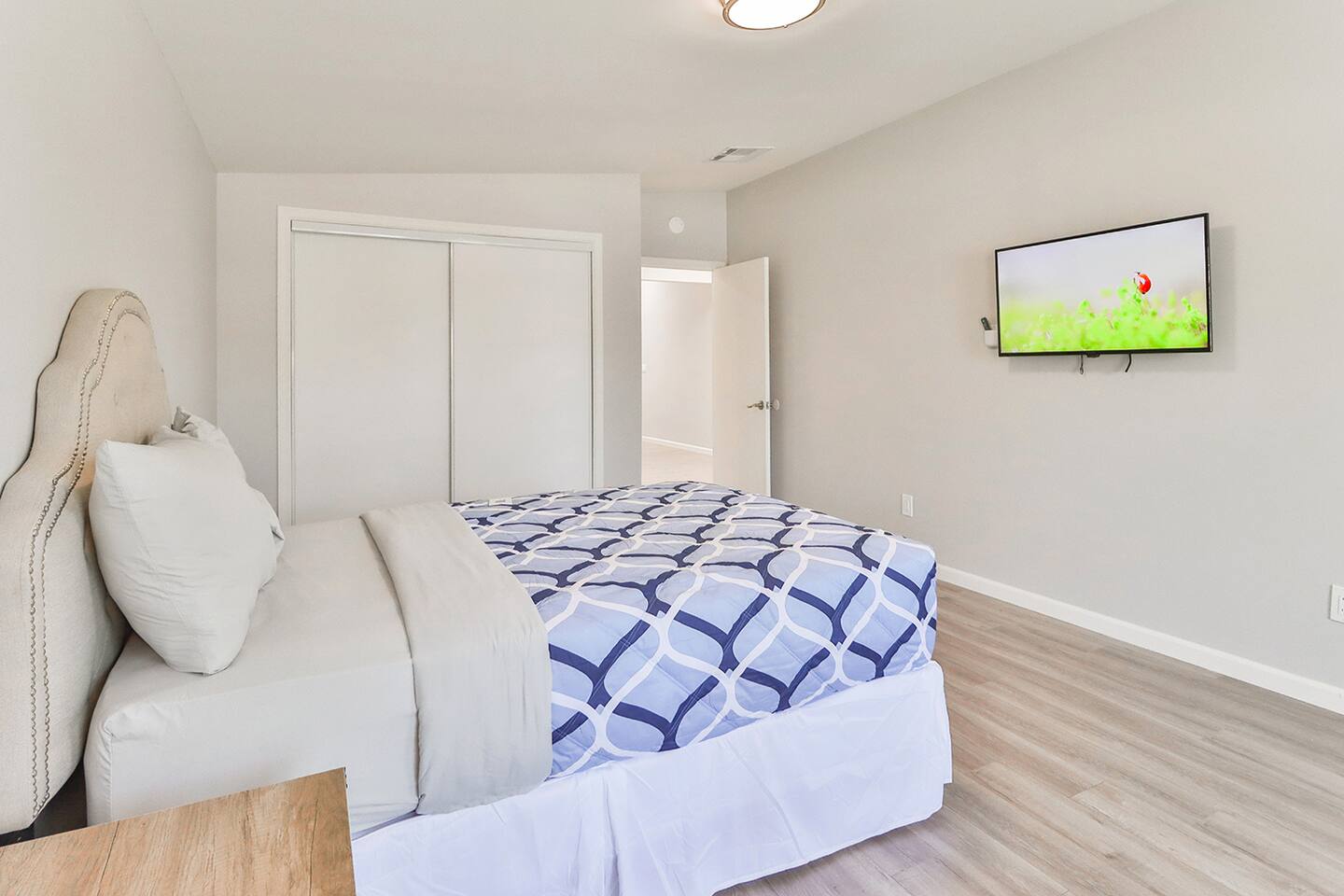 A cozy bedrooms features a bed, a mounted television and a closed white closet.