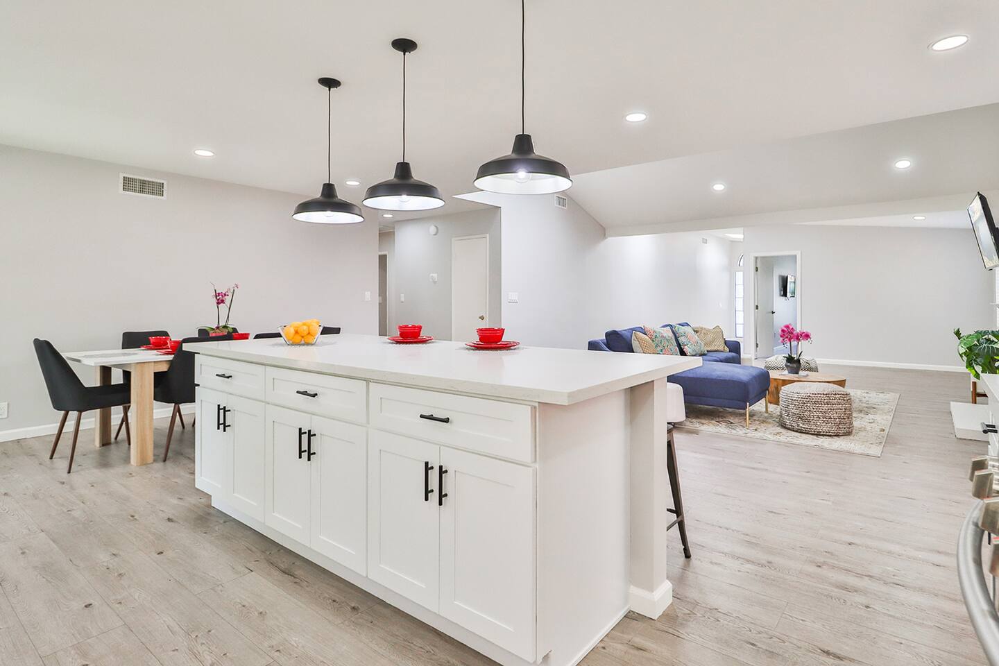 The bright kitchen island with its white countertop and cabinets, features open drawers revealing organized cutlery and utensils, all within an open-concept space that includes a dining area and living room.