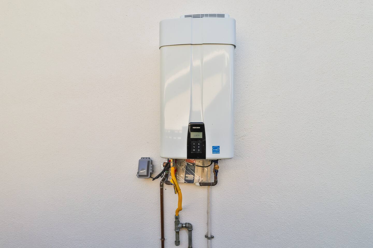 Efficient exterior-mounted tankless water heater system featuring a digital display, Energy Star certification, and professional installation on a clean white stucco wall.