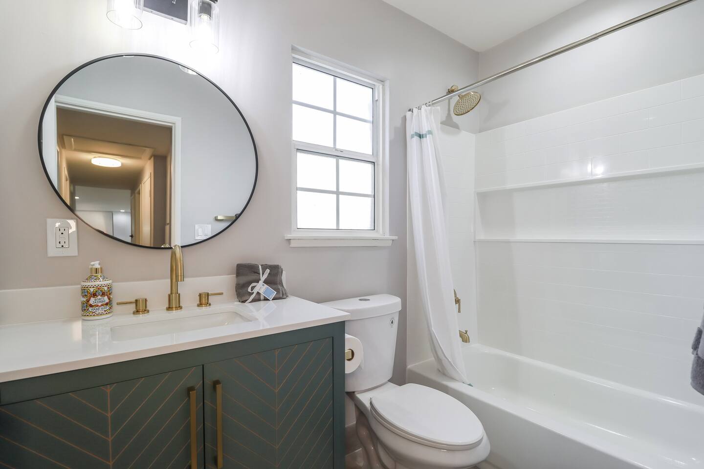 This modern bathroom features a stylish sage green vanity with gold chevron accents, a circular mirror, and a walk-in shower showcasing a mix of marble-style and green vertical subway tiles.