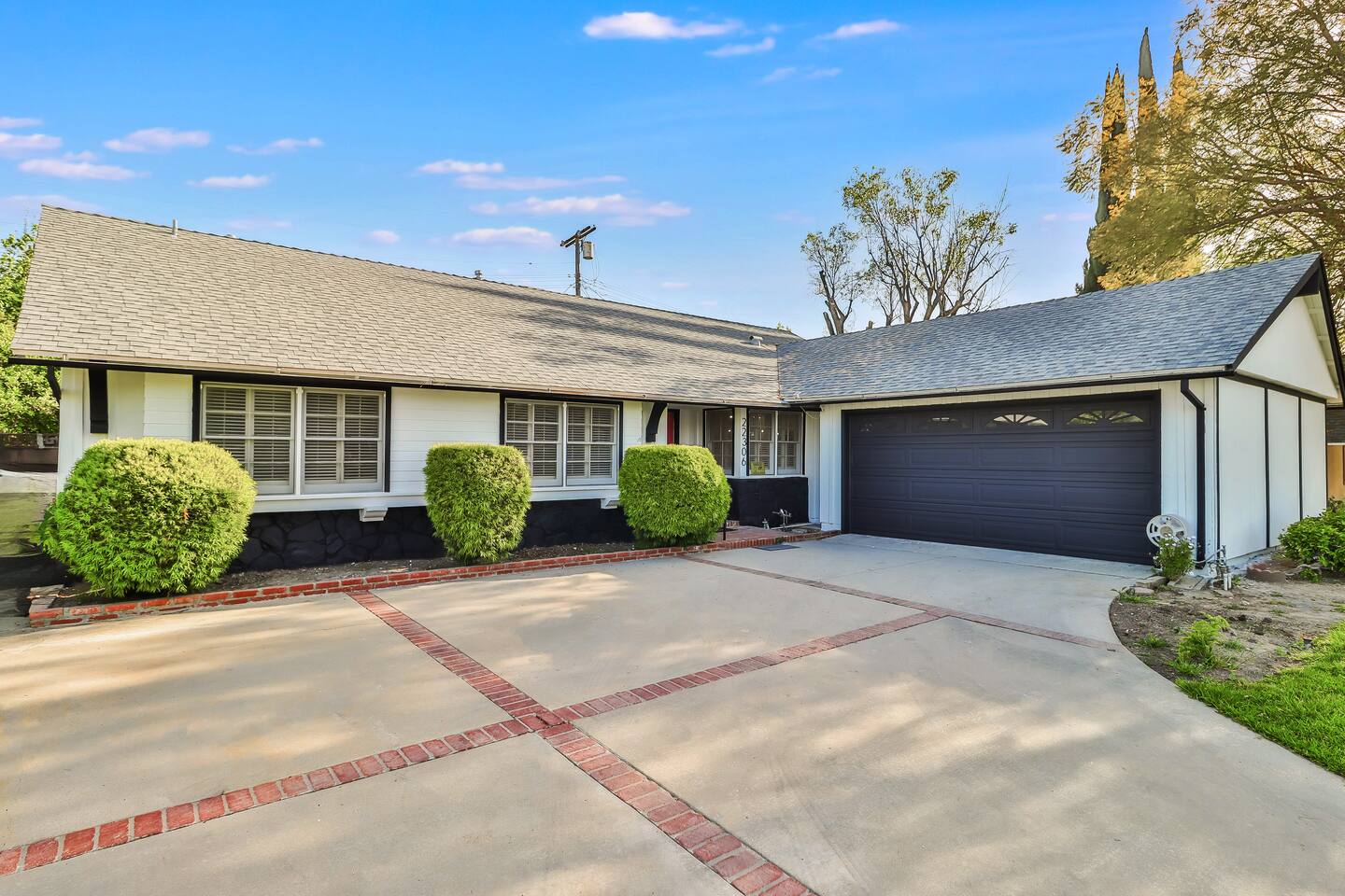 modern ranch-style home with a crisp white and black facade, a large two-car garage, and a manicured lawn with a spacious concrete driveway.